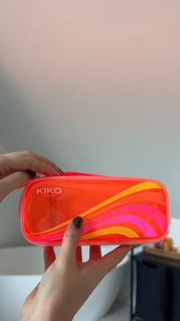 Przezroczyste etui na kosmetyki z jaskrawo pomarańczową podstawą, zdobione kolorowymi falami w odcieniach różu, żółci i pomarańczy. Zapięcie na zamek błyskawiczny u góry.