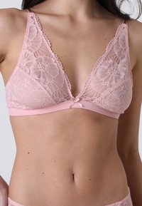Bralette in pizzo rosa con un motivo floreale, design con scollatura a V profonda e rifiniture in morbido satin. Presenta spalline regolabili e un fiocchetto al centro.