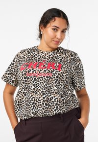 T-shirt con stampa leopardata in beige e nero con scritta rossa "CHÉRI toujours". Maniche corte, collo rotondo e vestibilità morbida. Morbido cotone.