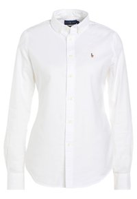 Vit, kragskjorta med knappar, långärmad, tillverkad av bomull. Har en liten broderad logotyp på vänster bröst och en rak fåll.