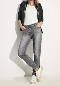 Jean gris en denim, avec une coupe slim, un délavage subtil et des poches avant. Assorti à des baskets blanches et un hoodie zippé noir.