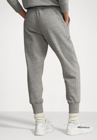 Sive trenirka iz mehkega materiala s tapered leg obliko, ki ima stranske žepe in rebraste manšete, v kombinaciji z belimi supergami.