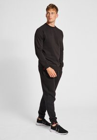 Sort sweatshirt med rund hals og lange ærmer, der er parret med sorte joggers. Inkluderer røde accenter og teksturerede sorte sportsko.
