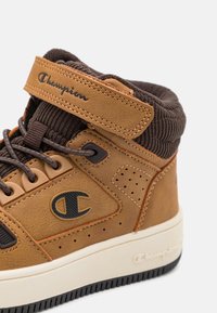 Sneaker alto marrone e beige con lacci marroni, cinturino in velcro, colletto imbottito e logo Champion sul lato e sulla suola.