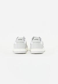 Sneaker bianche e grigie chiare presentano una tomaia in pelle liscia, punta arrotondata e suola in gomma texturizzata. Marchio visibile sul tallone.