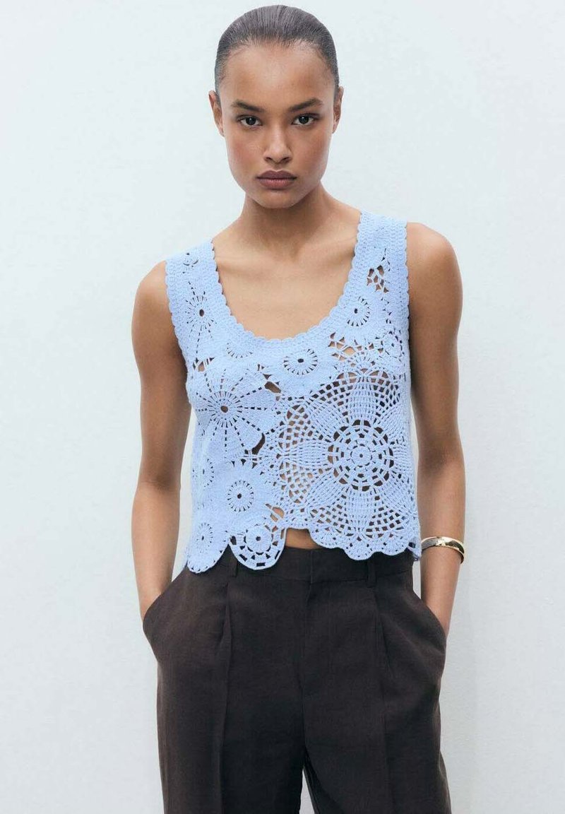 Top in cotone all'uncinetto di colore azzurro chiaro con motivi floreali e orlo a scallop, abbinato a pantaloni scuri a vita alta marroni. Tessuto morbido e vestibilità ampia.