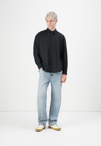 Chemise à carreaux noire à boutons avec col et poche, associée à un jean droit bleu clair et des baskets crème. Fond uni.