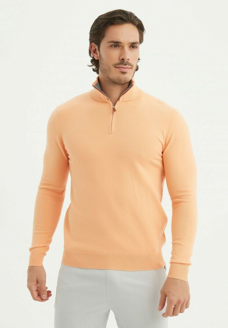 Pull en maille pêche clair avec un col zippé mi-long, des manches longues et des poignets et un ourlet côtelés. Texture lisse, design minimaliste.