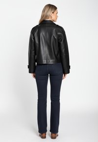 Zwarte leren jas met een getailleerd ontwerp, voorzien van gevormde schouders en manchetten met knopen, gecombineerd met donkerblauwe wijde spijkerbroeken en bruine laarzen.