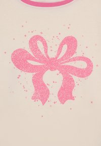Lys beige stoff med et stort rosa glitrende sløyfemotiv, omkranset av små rosa stjerner, med en lys rosa ribbestrikket halslinning.