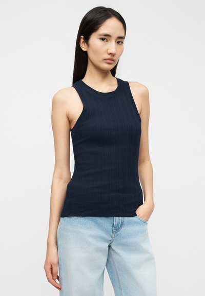 Μπλε ναυτικό ριπτό αμάνικο τοπ με στρογγυλή λαιμόκοψη και χωρίς μανίκια, σε συνδυασμό με ανοιχτόχρωμο τζιν παντελόνι. Λείο υφή και εφαρμοστή σιλουέτα.
