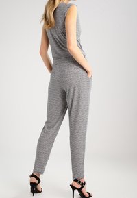 Combinaison à motifs noir et blanc avec un design sans manches ; taille ajustée et jambes fuselées ; associée à des sandales à talons hauts noires.