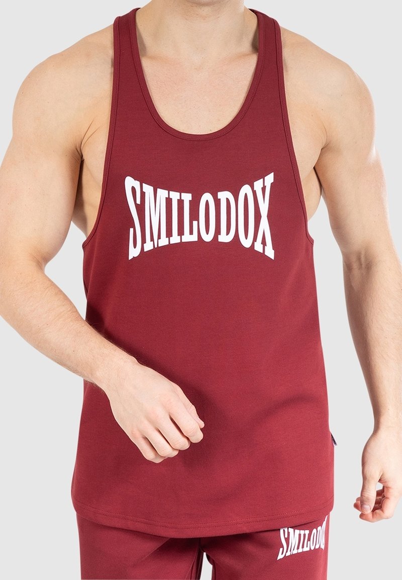 Personne musclée portant un débardeur bordeaux sans manches et un short assorti, tous deux imprimés du mot « SMILODOX » en blanc.