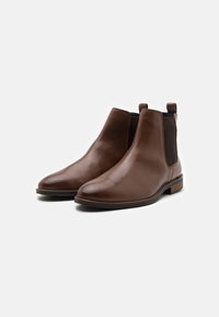 Hnědé kožené chelsea boty s elastickými bočními panely, zaoblenou špičkou a malým podpatkem. Elegantní design s hladkým povrchem a minimálními akcenty.