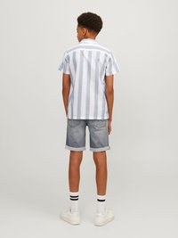Chemise à manches courtes rayée bleu clair et blanche, associée à un short en denim retroussé, des baskets blanches et des chaussettes rayées noir et blanc.