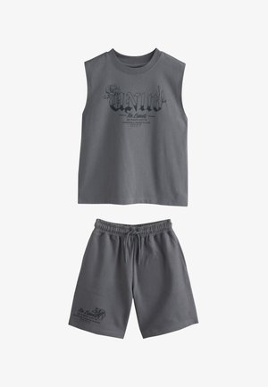 Camiseta sin mangas de color gris oscuro con texto y gráfico "Unity", combinada con pantalones cortos a juego con cintura elástica que presentan texto pequeño y diseño de flores.