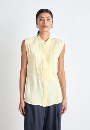 Kortærmet, lys gul bluse med plisseret front, knaplukning og krave. Fremstillet af et let materiale med en glat tekstur.