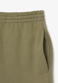 Pantalones de chándal verde oliva con una cintura elástica, bolsillos laterales y una textura suave. Presenta un diseño simple y sin adornos.