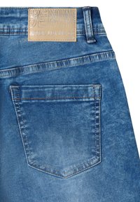 Poche arrière d'un jean en denim bleu avec une couture visible et une étiquette en cuir beige portant l'inscription « DENIM NEVER LET ME GO. »