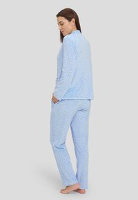 Conjunto de pijama azul claro en tela suave, con un patrón de puntos, manga larga y pantalones con bolsillos laterales. Diseño simple, corte relajado.