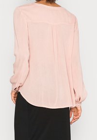 Blusa rosa clara con mangas largas, un escote redondeado y un dobladillo ligeramente curvado. Presenta un tejido texturizado y un ajuste relajado.