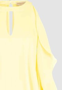 Blusa gialla con scollo a goccia, maniche lunghe e tessuto morbido. Presenta pieghe sottili e una texture liscia. Etichetta visibile all'interno dello scollo.
