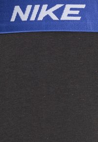 Sorte atletiske leggings med en blå elastisk talje, der har hvid "NIKE" tekst. Stoffet er glat med en let struktur.