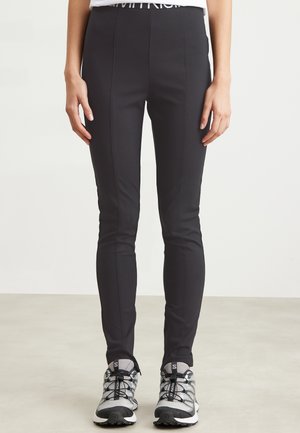 Leggings noirs extensibles avec une taille haute et des coutures verticales, associés à des chaussures de sport grises avec des accents noirs et des lacets.