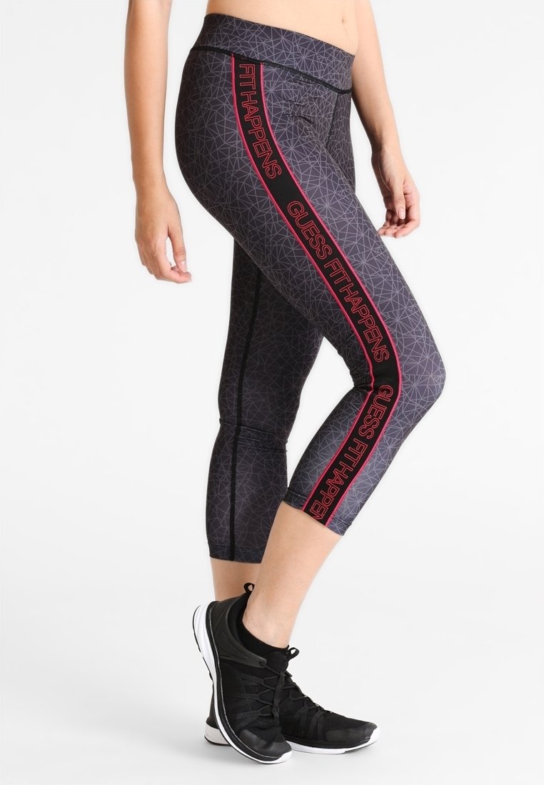 Svarta capri leggings med ett geometriskt mönster, som har en röd grafisk textdesign längs de yttre sömmarna. Tillverkade av ett elastiskt, lätt material.