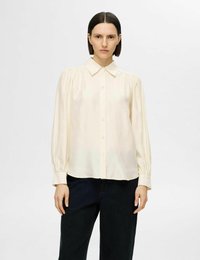 Ljus krämfärgad skjorta med knappar, lång ärm med volanger och klassisk krage, parat med mörk denimbyxor. Slät tygstruktur.