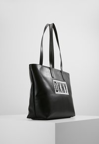 Černá kožená taška přes rameno s čtvercovým mřížkovým vzorem a logem na přední straně. Má dlouhé, ploché popruhy a strukturovaný tvar.