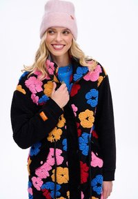 Pestrofarebná fleecová bunda s kvetinovým vzorom na čiernom základe, obsahujúca ružové, oranžové, modré a červené kvety; zapínanie na zips a bočné vrecká.