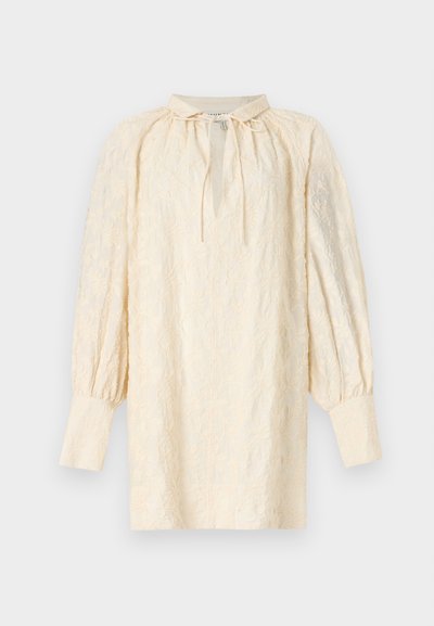 Κρεμ πουκάμισο μακρυμάνικο με κεντήματα λουλουδιών, φαρδιά μανσέτα, μικρό γιακά και λαιμόκοψη με κορδόνι στο μπροστινό μέρος, παρουσιάζεται σε λευκό φόντο.