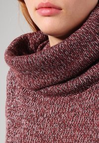 Pull en maille bourgogne avec un grand col roulé replié, présentant un motif texturé et un mélange de fibres claires et foncées.