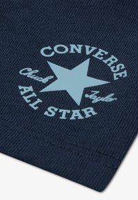 Ύφασμα ναυτικού μπλε με υ φαντή υφή που περιλαμβάνει ένα ανοιχτό μπλε κυκλικό λογότυπο. Το λογότυπο περιλαμβάνει ένα αστέρι και τις λέξεις "CONVERSE Chuck Taylor ALL STAR".