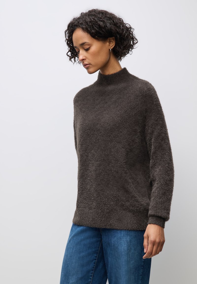 Maglione marrone scuro morbido con un collo alto e una vestibilità rilassata. Presenta maniche lunghe e una superficie tessurizzata, abbinato a jeans blu.