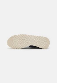 Suela de zapato con un patrón texturizado y estriado en crema y negro. Destacan los agarres circulares y triangulares que mejoran la tracción.