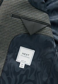 Tailored jacket featuring a houndstooth pattern in brown and blue tones, with a dark navy lining and a slim fit label from NEXT.