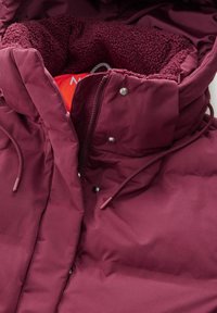 Bordo napihljiva jakna s teksturiranim flisom. Ima visok ovratnik, sprednji zadrgo, gumbke na zapiranje in prilagoditve s vrvico.