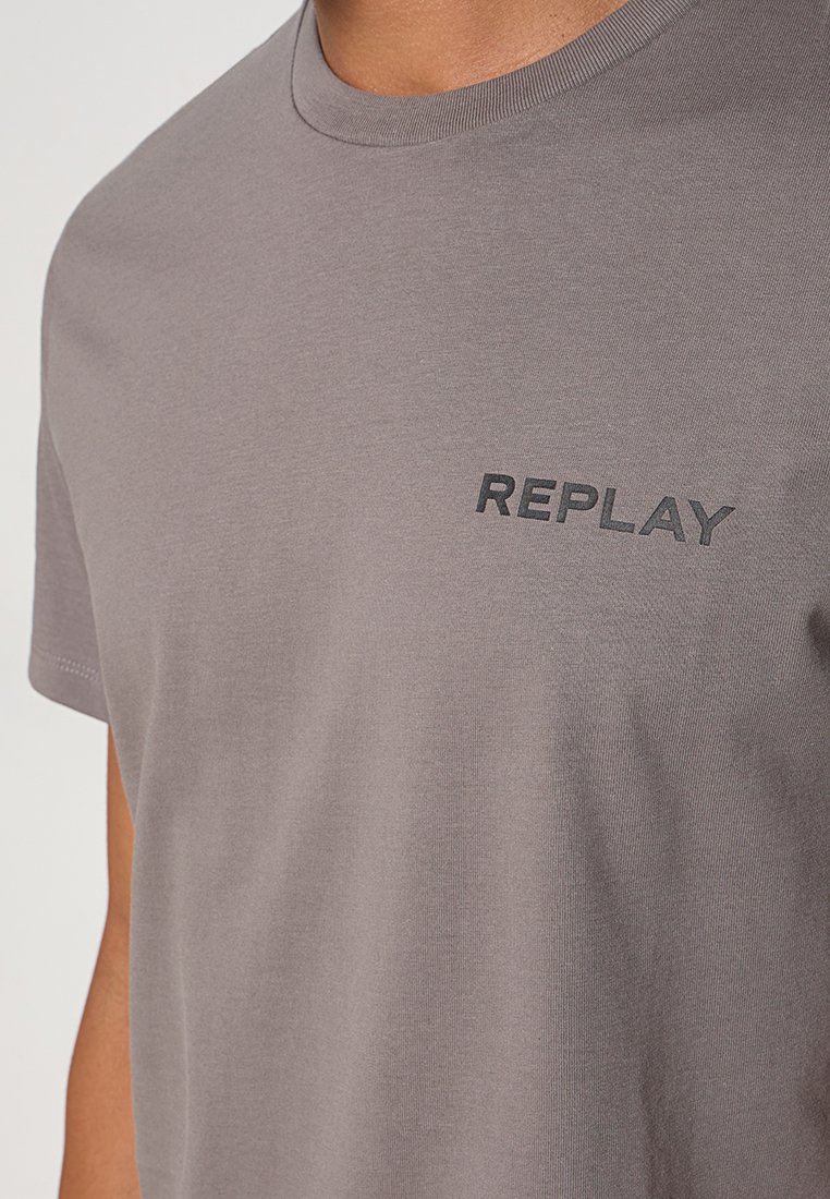 Graues Baumwoll-T-Shirt mit kurzen Ärmeln, das ein schwarzes "REPLAY"-Logo im linken Brustbereich trägt. Glatte Textur und Rundhalsausschnitt-Design.