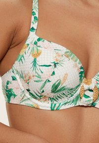 Bikini top s drôtikmi, ktorý má biely kvetinový vzor so zelenými listami a jemnými zlatými akcentmi, doplnený o pletený béžový uzlík.