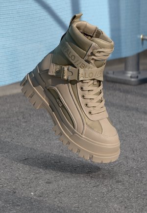 Beige lace-up boots with a high ankle, textured leather and mesh panels, featuring a chunky sole and a strap with logo detail.