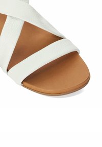 White leather sandal with crisscross straps, a smooth finish, and a tan flat sole. Designed for comfort and casual wear.
