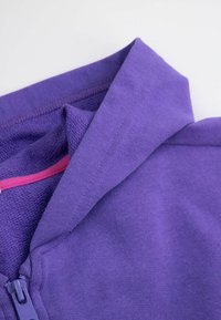 Fioletowa kurtka na zamek o miękkiej teksturze. Posiada złożony kołnierz oraz kontrastujący różowy akcent wzdłuż zamka.