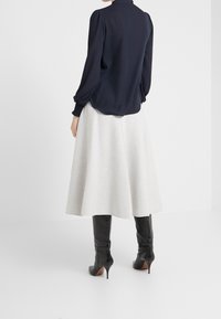 Námořnická halenka s nadýchanými rukávy, kombinovaná se světle šedou áčkovou sukní a černými kozačkami ke kolenům, vyznačující se hladkou texturou a střižením na míru.