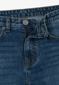 Jeans in denim indaco con finitura sbiadita, dotati di un bottone per la chiusura, un particolare bottone in metallo e cuciture beige lungo le cuciture e le tasche.