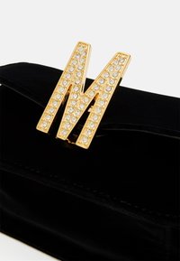 Pochette en velours noir avec une broche "M" dorée ornée de strass clairs sur le rabat avant.