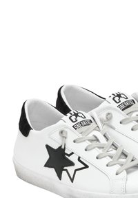 Sneaker bianchi basse con design a stella nera sul lato, lacci grigi e dettaglio nero sul tallone. Logo "SNEAKER?" sulla linguetta.