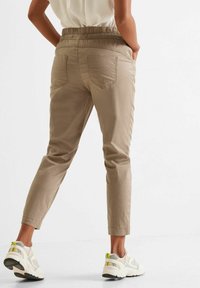 Pantalones marrón claro, ajustados y con cintura elástica. Dos bolsillos traseros, dobladillos enrollados, combinados con zapatillas blancas y amarillas.