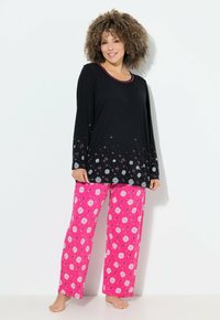 Černý top s dlouhým rukávem a růžovým lemem, zdobený bílými a růžovými květinovými vzory; spárovaný s růžovými pyžamovými kalhotami s květinovými motivy.